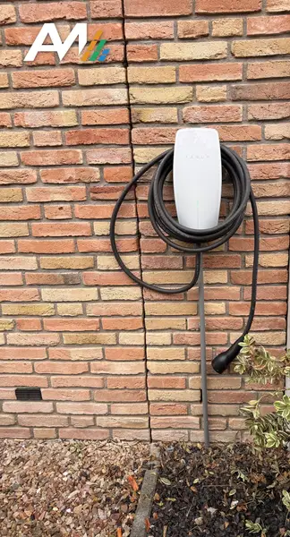 Tesla Wall Connector met opgerolde kabel aan een bakstenen gevel